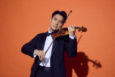Ray Chen playing violin in a tuxedo on an orange background