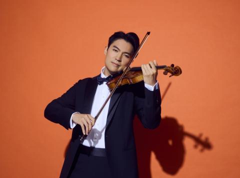 Ray Chen playing violin in a tuxedo on an orange background